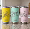 Three YETI tumblers in yellow, blue, and pink with bird illustrations on a kitchen counter.
