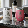 Two YETI brand wine tumblers, one white and one pink, on a table with a bottle of wine in the background. Laser Engraved Designs